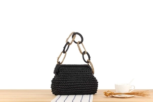 Close-up of black woven handbag featuring a chunky black and gold chain handle detail