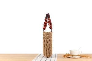 Detail of handmade cylindrical straw bag with deep red beaded wood handle on table