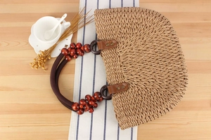 Detail of semi-circular straw handbag with wooden beads and woven rope handle on wood