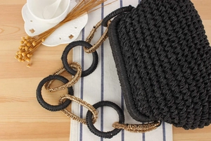 Detail of black woven bag featuring a stylish black and gold ring-linked shoulder strap