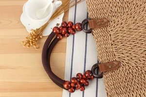 Detail of woven straw bag handle with reddish-brown wooden beads and leather reinforcement