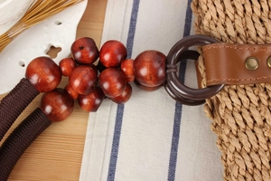Detail of woven straw bag featuring red wood beads and leather strap with metal rivets