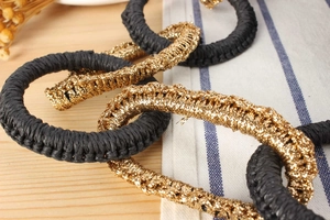 Close-up of interconnected black straw and metallic gold woven rings on a wooden desk