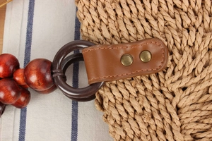 Close-up of woven straw bag with leather trim, bronze rivets and wooden bead strap detail