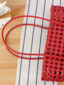 Red woven hollow-out basket handbag with long handles on a wooden table setup