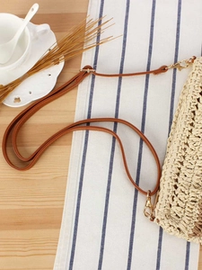 Chic woven straw handbag with brown leather strap on a blue and white striped fabric