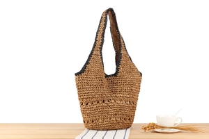 Detailed view of handmade woven straw tote bag with black trim on a summer table setting
