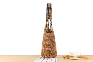 Detail of hand-woven straw tote with black contrast handles and hollow mesh texture