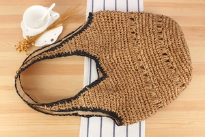 Top view of handwoven straw tote bag with black trim on a wooden table with coffee cup
