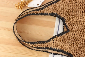 Detail of woven straw tote bag with black edge accents on a rustic wooden table background
