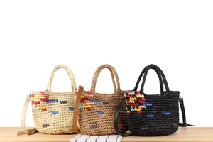 Detail of three woven tote bags in beige, brown and black with colorful floral embroidery