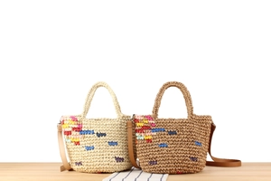 Detail of hand-woven straw bucket bag featuring colorful abstract floral embroidery and leather strap