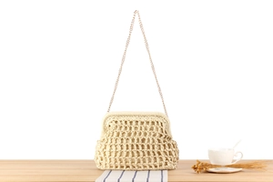 Close-up of cream woven shoulder bag with gold chain strap on a rustic wooden table