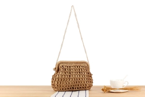 Detail of woven straw bag with gold chain strap on wooden surface for beach vacation style