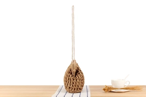 Detail of a brown woven bucket bag with a gold metal chain strap on a rustic tabletop