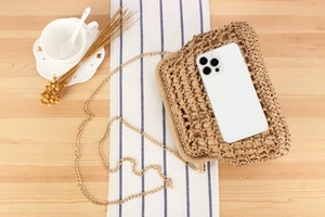 Macro detail of beige woven straw bag with gold chain strap and phone for size scale