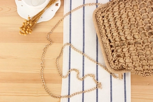 Detailed top view of a woven straw bag with a gold chain strap on a rustic table