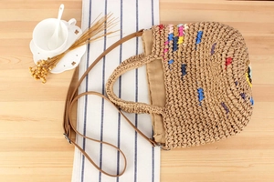 Detail of colorful hand-woven straw bag with leather straps on a wooden table setup