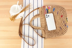 Detail of woven straw handbag with colorful embroidery and brown leather strap on table