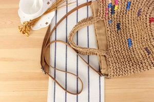 Detail of woven straw handbag featuring colorful accents and adjustable leather strap