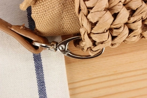 Detail of woven bag with brown leather strap and silver metal clasp on wooden background