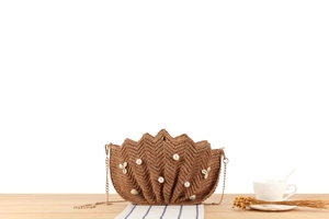 Detail of raffia woven bag with pearl and shell accents on a wooden surface