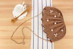 Detail of brown raffia woven bag with pearls, shells, and elegant gold chain strap