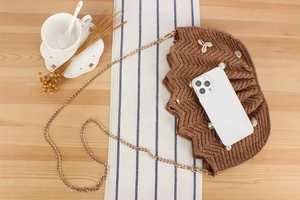 Detail of raffia woven crossbody bag featuring seashell and pearl embellishments and chain
