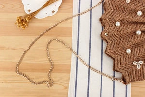 Detail of raffia woven bag with scalloped texture, faux pearls, shells and gold chain