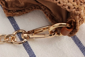 Detail of raffia woven bag featuring gold metal hardware and delicate chain strap