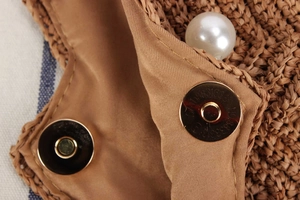 Detail of raffia woven bag with magnetic gold clasp, inner lining, and pearl accent