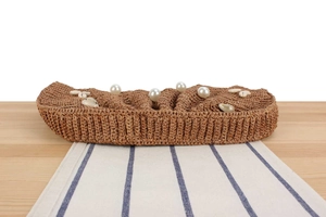Macro detail of raffia woven clutch bag with pearl and shell accents on wooden table