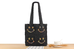 Detail of a black woven tote bag with a colorful beaded smiley face on a wooden table
