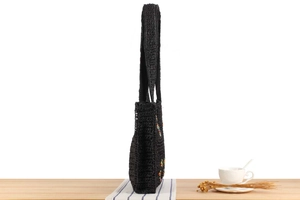 Detail of a handmade black woven tote bag with colorful beads on a wooden table