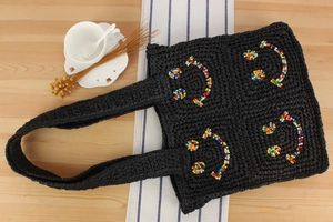 Detail of black woven tote bag with colorful beaded smiley faces on wooden surface