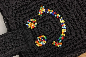 Close-up of black woven bag featuring a colorful beaded smiley face detail