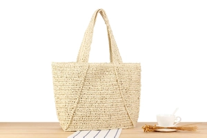Detail of large beige woven tote bag with triangular stitching on light wood surface