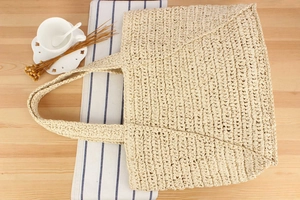 Flat lay of woven straw tote bag on wooden table with seaside vacation accessories