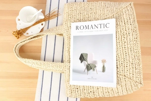Detail of cream woven tote bag with long handles on a casual vacation style tabletop