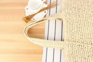 Flat lay of a large woven straw tote bag with dense texture on a cozy wooden table