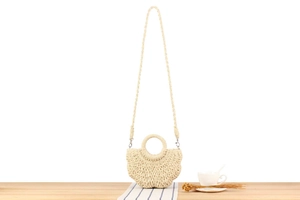 Close-up of beige woven straw handbag with a round handle on a wooden table setup