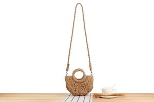 Detail of hand-woven semi-circle straw bag with circular handle and thin strap