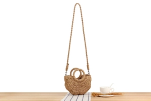 Detail view of a handcrafted crescent woven straw bag with circular handles on a wooden table