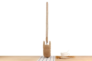 Detail of hand-woven straw crossbody bag with metal clasps on a rustic wooden table