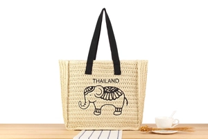 Detail of hand-woven straw tote bag with elephant pattern and black strap handles