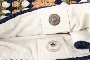 Detail of metal magnetic clasp and beige canvas lining on a hand-woven crochet bag