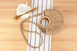 Detailed top view of a semi-circular straw woven bag with ring handle on wooden desk