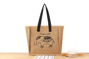 Detail view of woven straw tote bag featuring a black elephant print and Thailand lettering