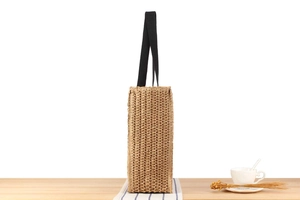 Side view of straw tote bag with black handles on a wooden table for summer
