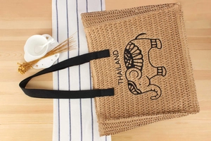Macro shot of a handmade straw tote bag featuring a black elephant embroidery and woven handles